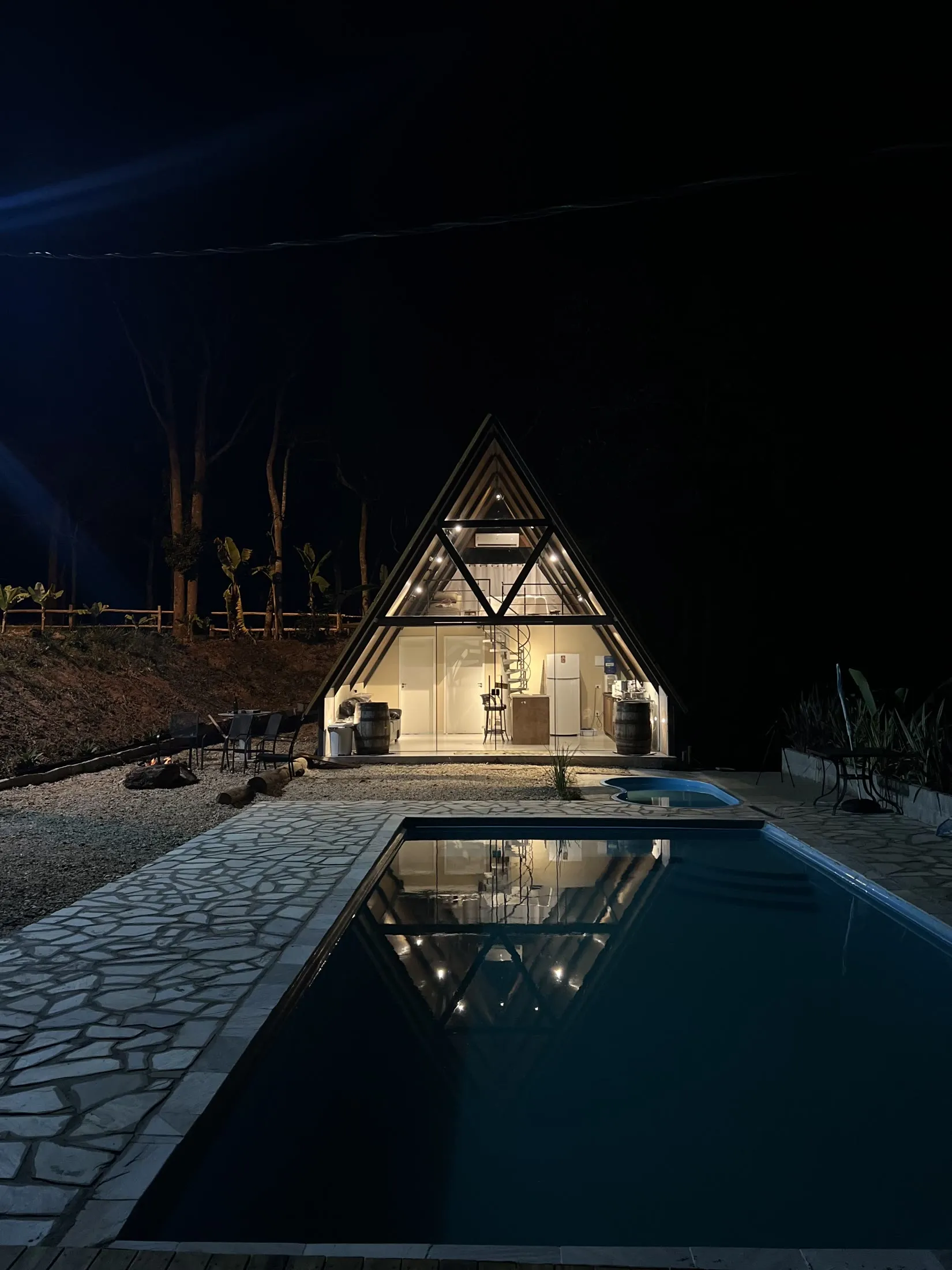O chalé iluminado à noite, refletido na piscina